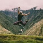 woman jumping on green mountains